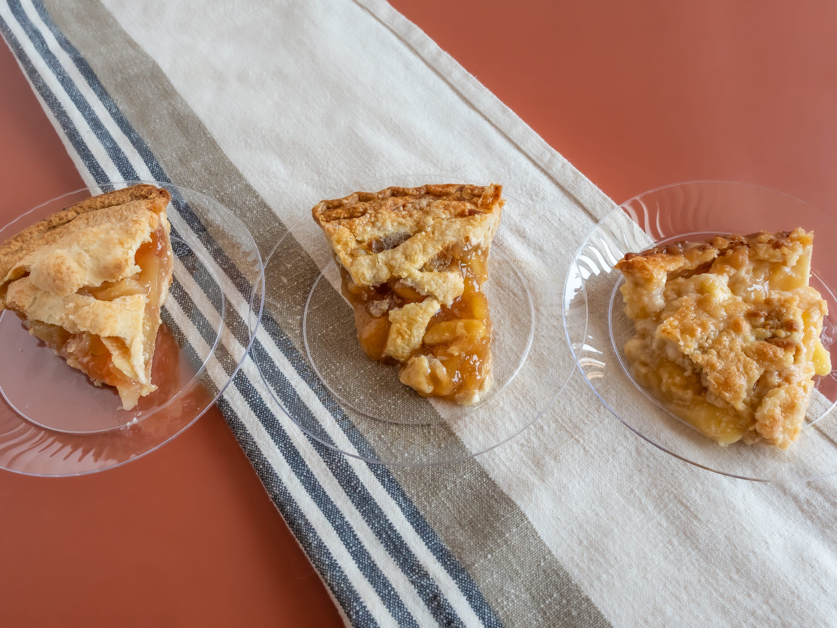 Three apple pie slices from Safeway, Whole foods, and Kroger on clear plates on table