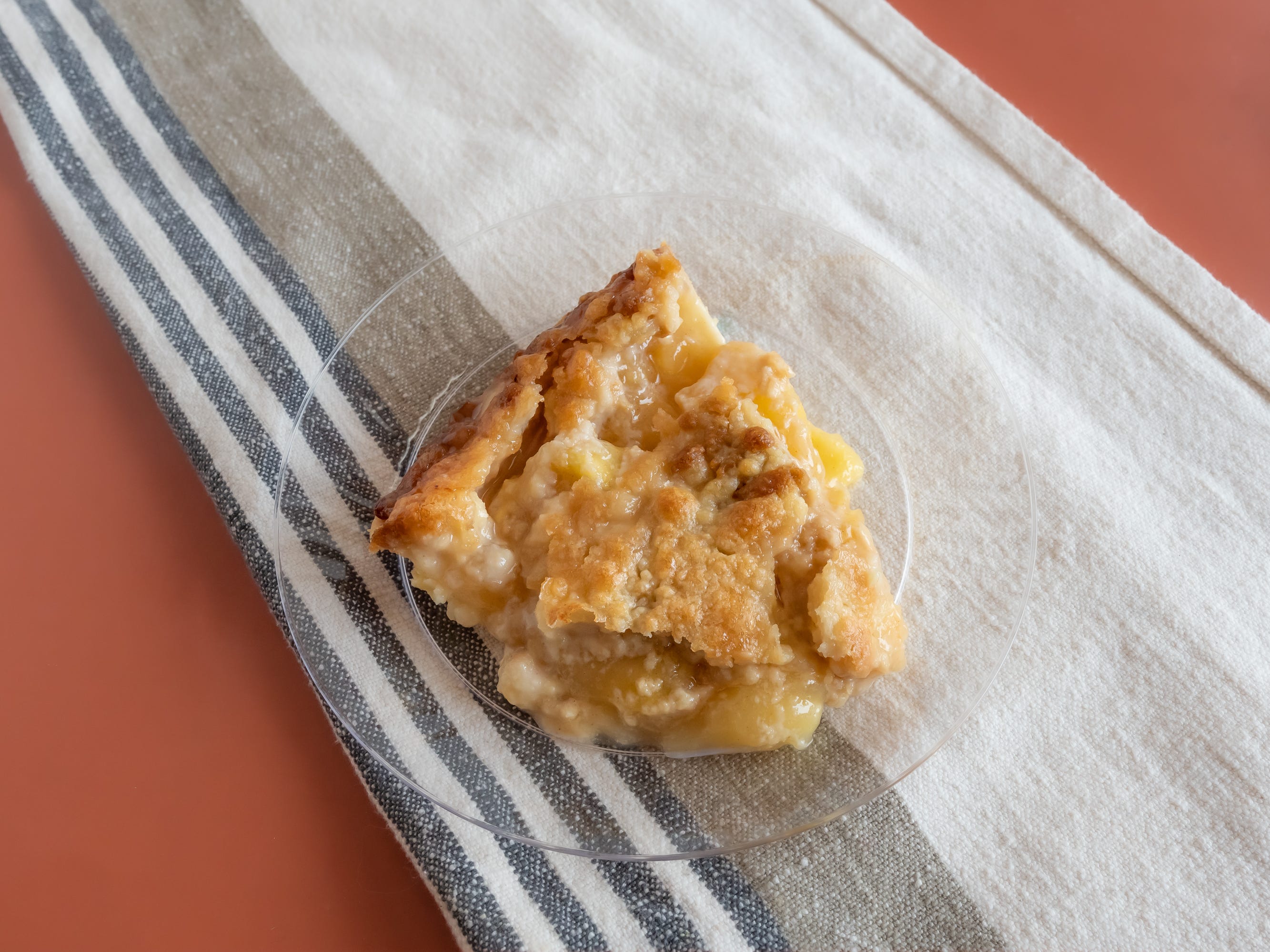 Slice of kroger apple pie on small clear plate on red table