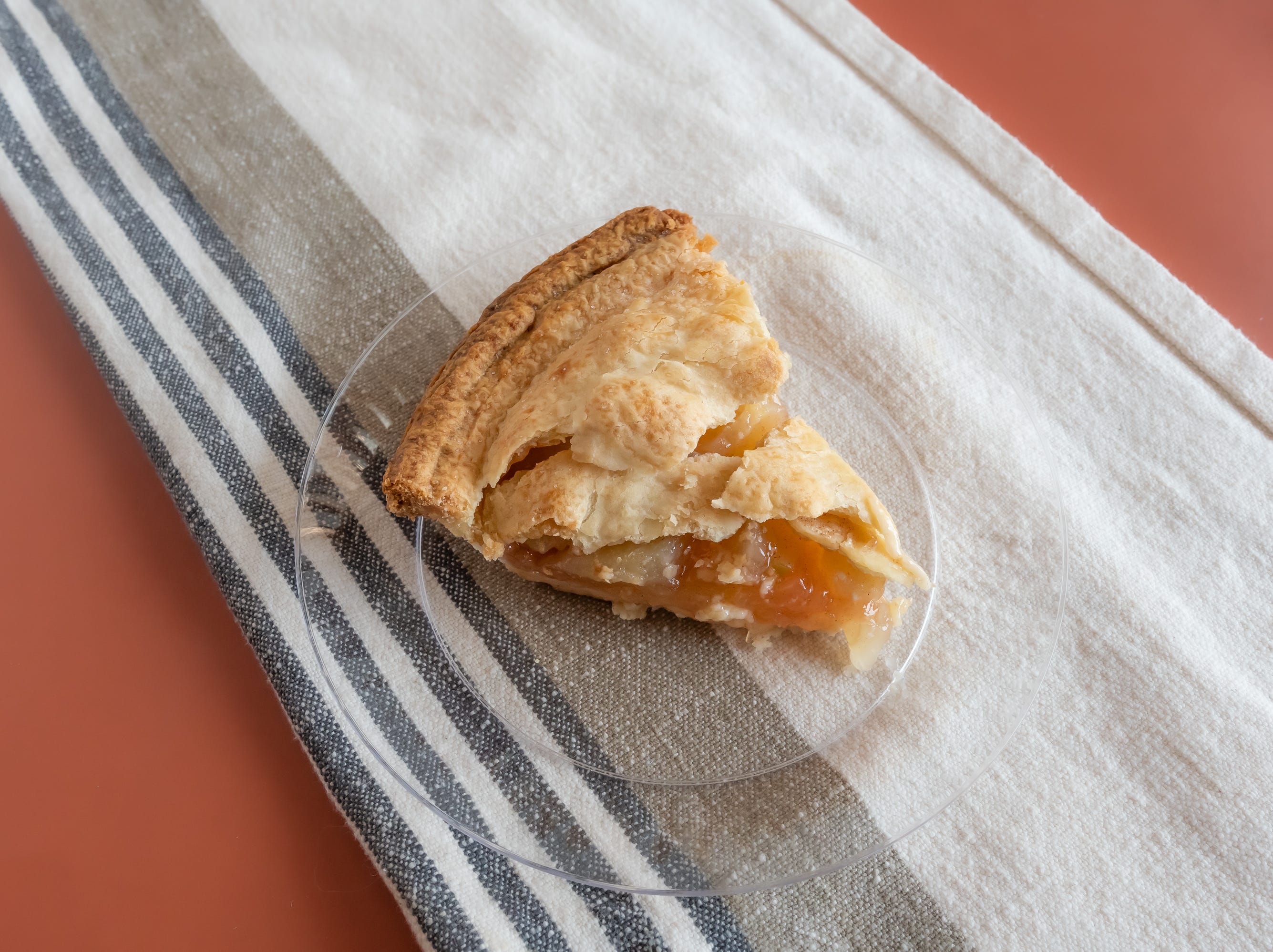 Slice of apple pie from whole foods on small clear plate on red table