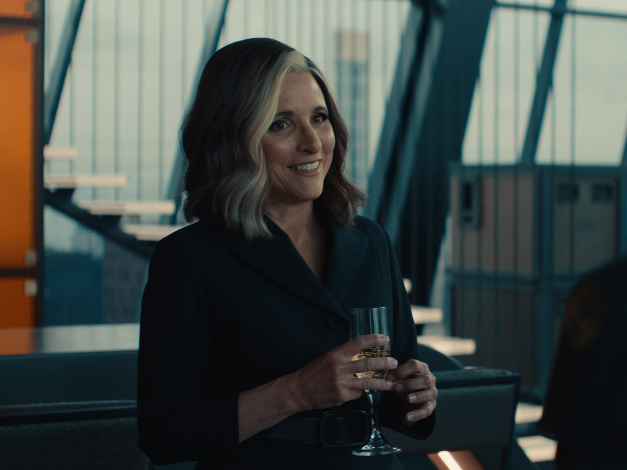 A still of "Thunderbolts*" showing Julia Louis-Dreyfus with white streaked hair holding a glass of bubbly.