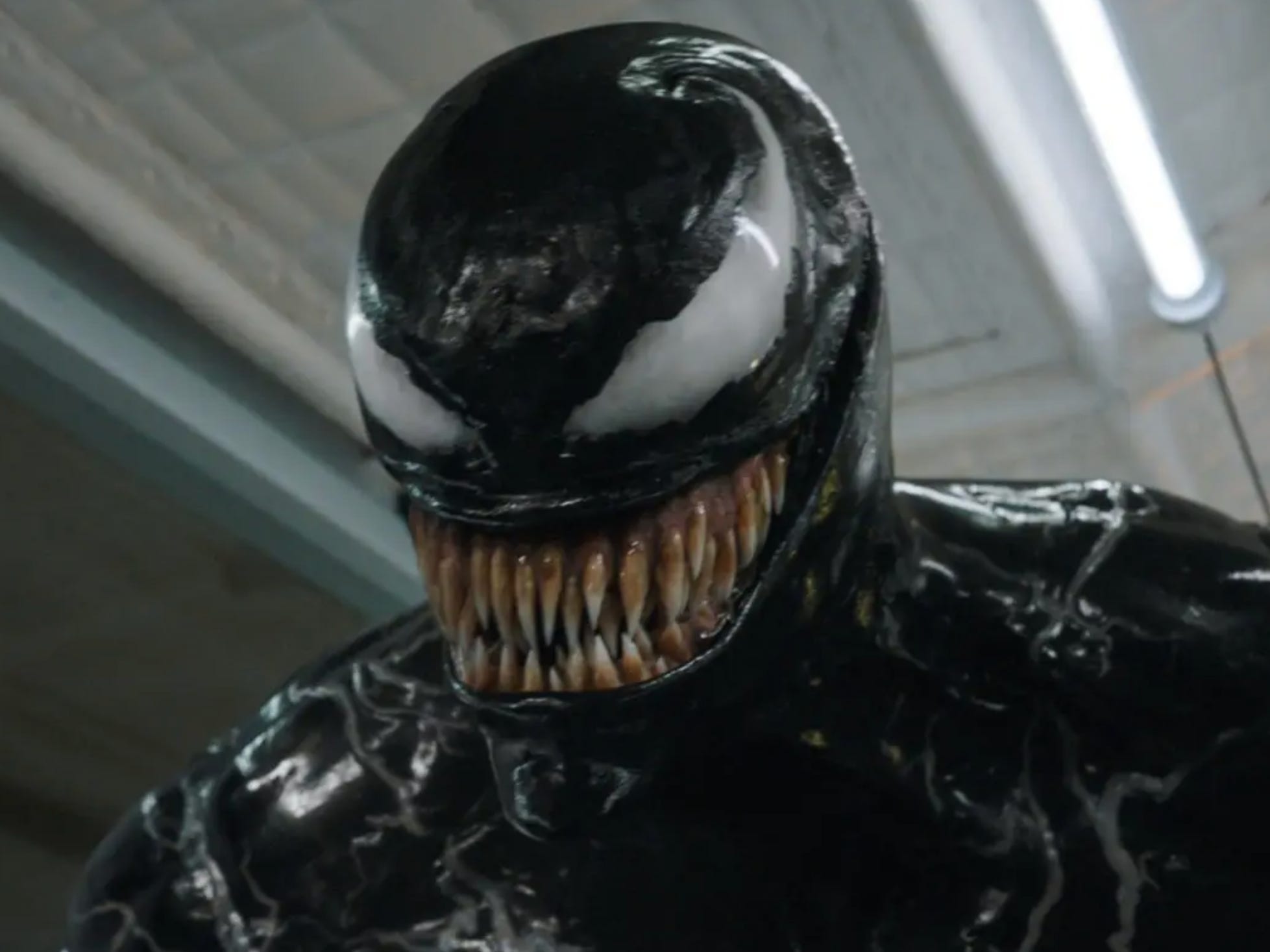 A black gooey alien with white eyes that curl up around its head. It has a large set of teeth protruding from its mouth.