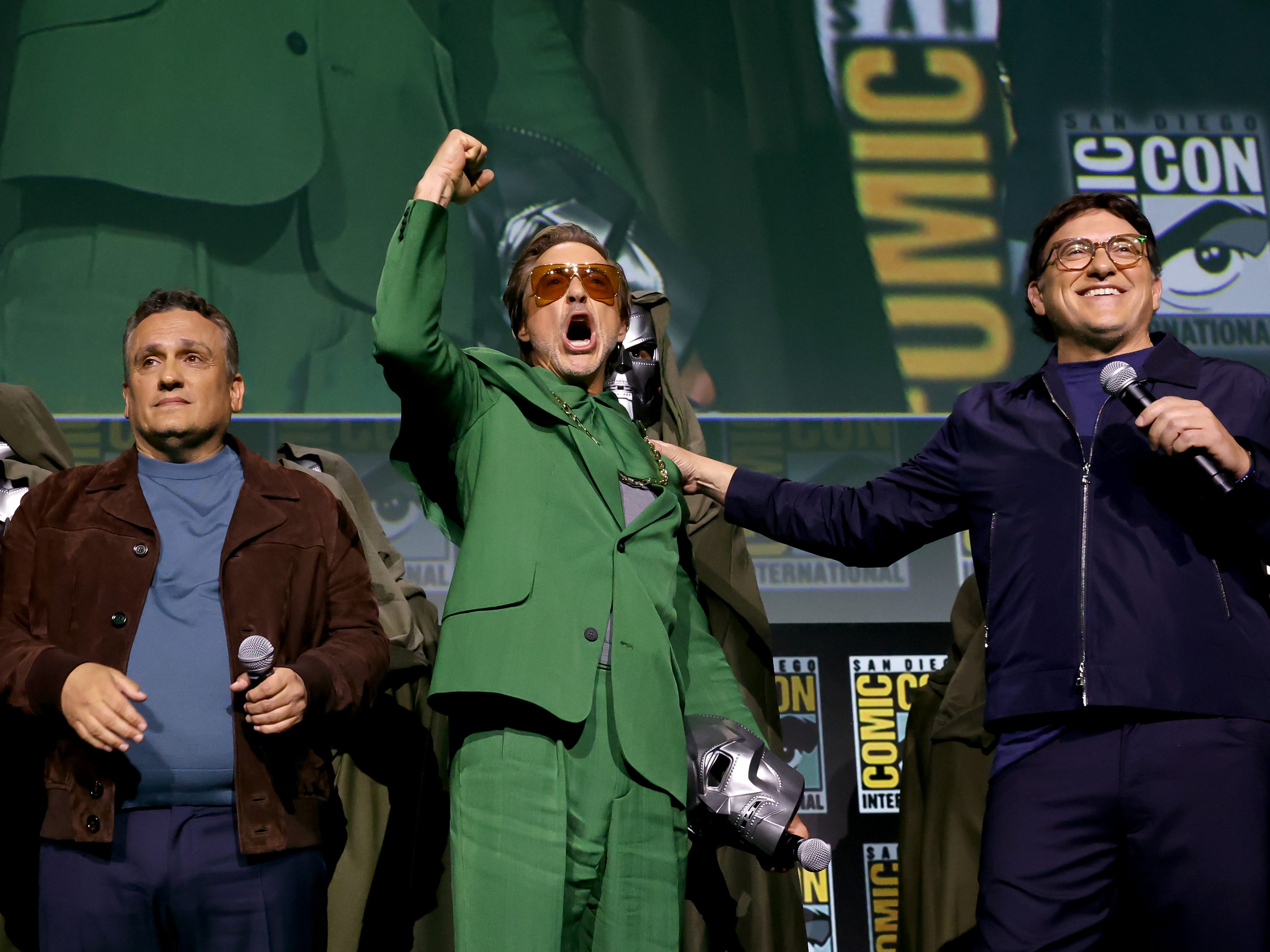 Joe Russo, Robert Downey Jr. with a fist raised up and Anthony Russo stand together at San Diego Comic Con in July 2024.