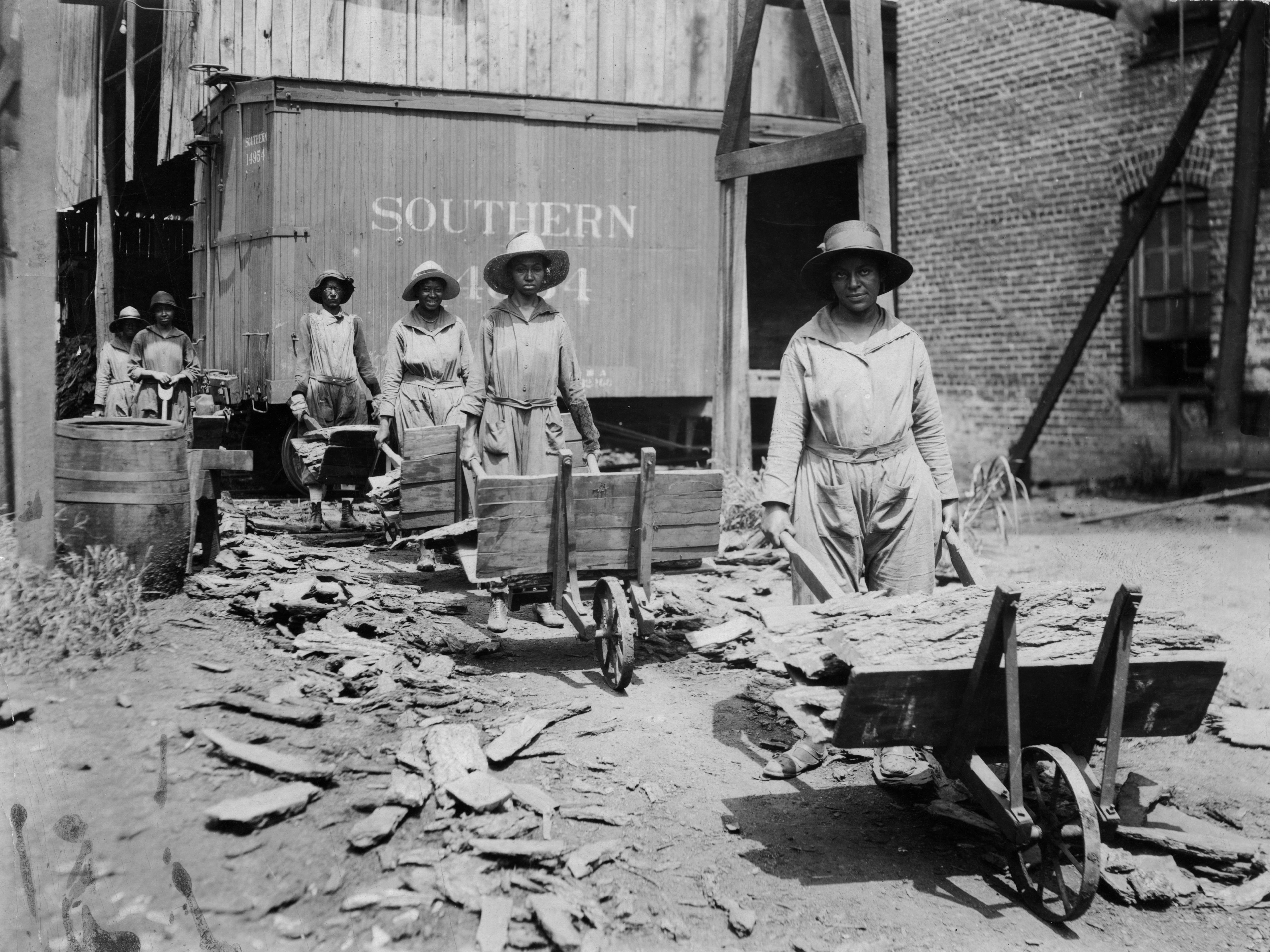 Black female construction workers in the South holding wheelbarrows of materials.