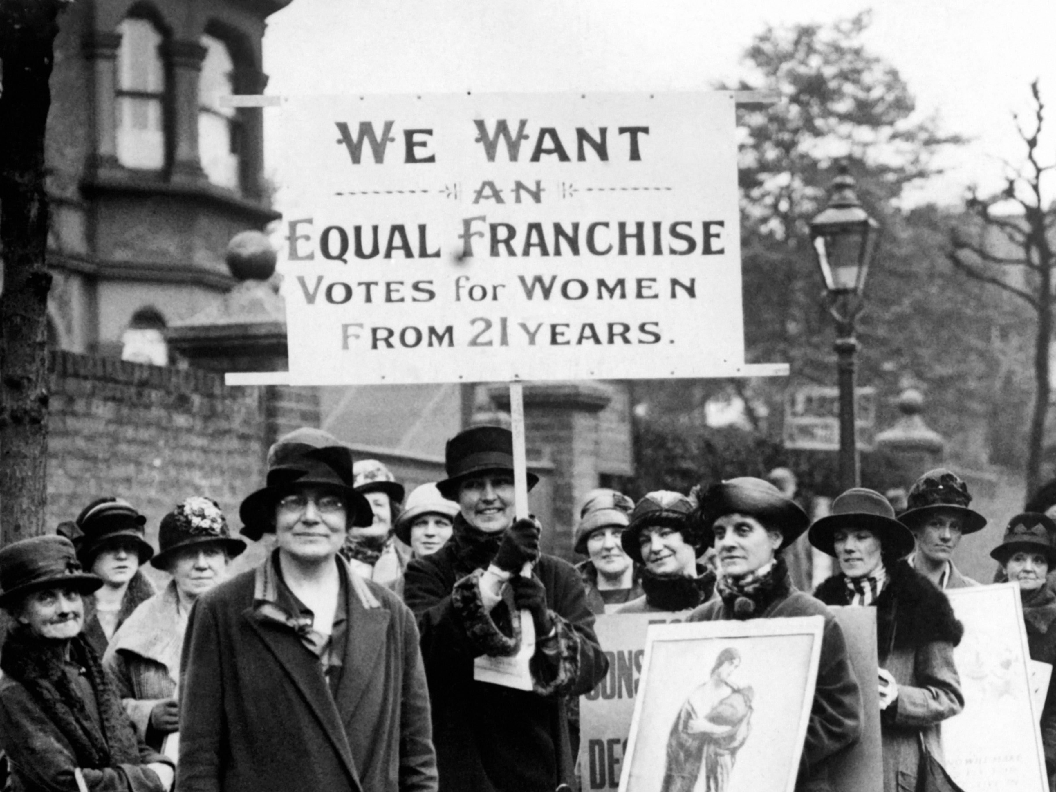 Labour Party Vice President Susan Lawrence, left, in front of a group of women protesting for the right to vote in London. Another woman holds a large sign that reads, "We want an equal franchise votes for women from 21 years."