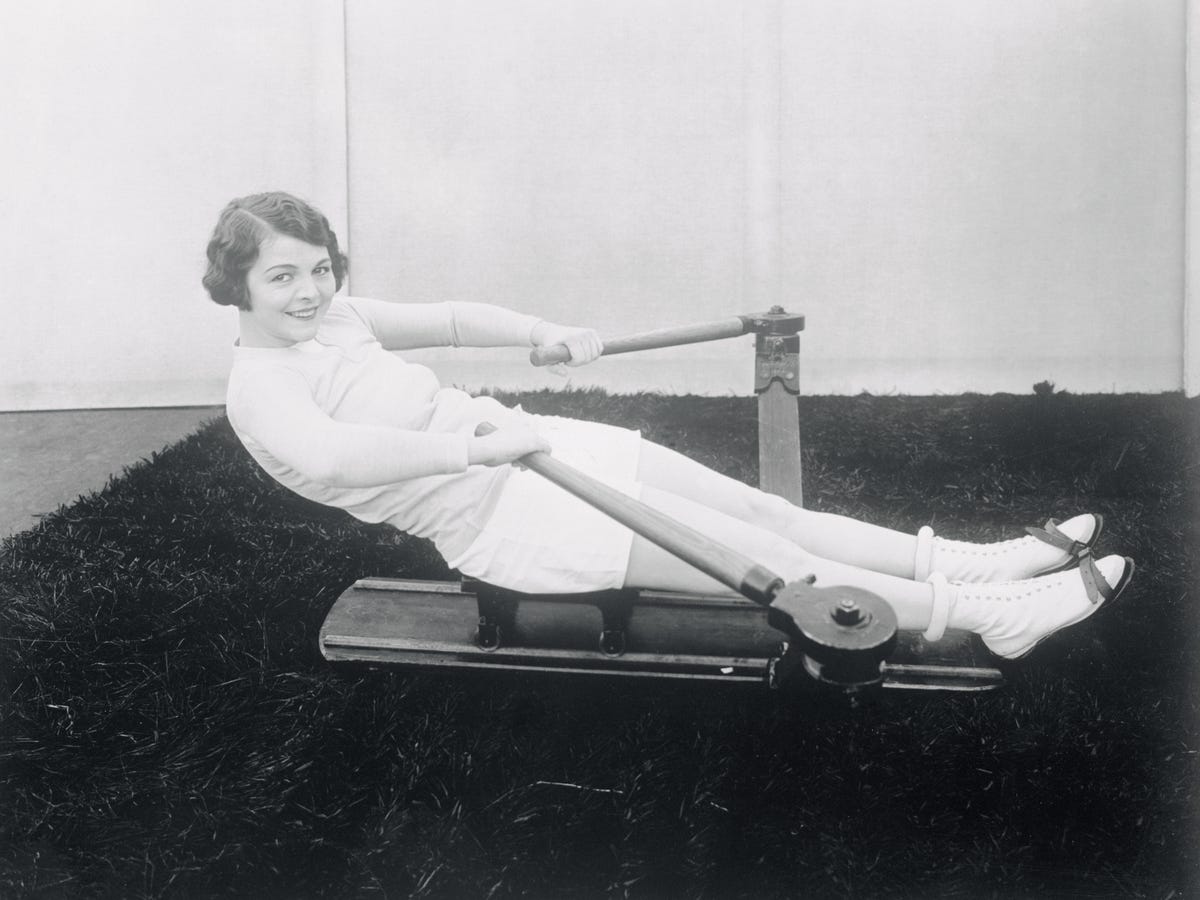Helen Chadwick smiling and using a 1920s rowing machine.