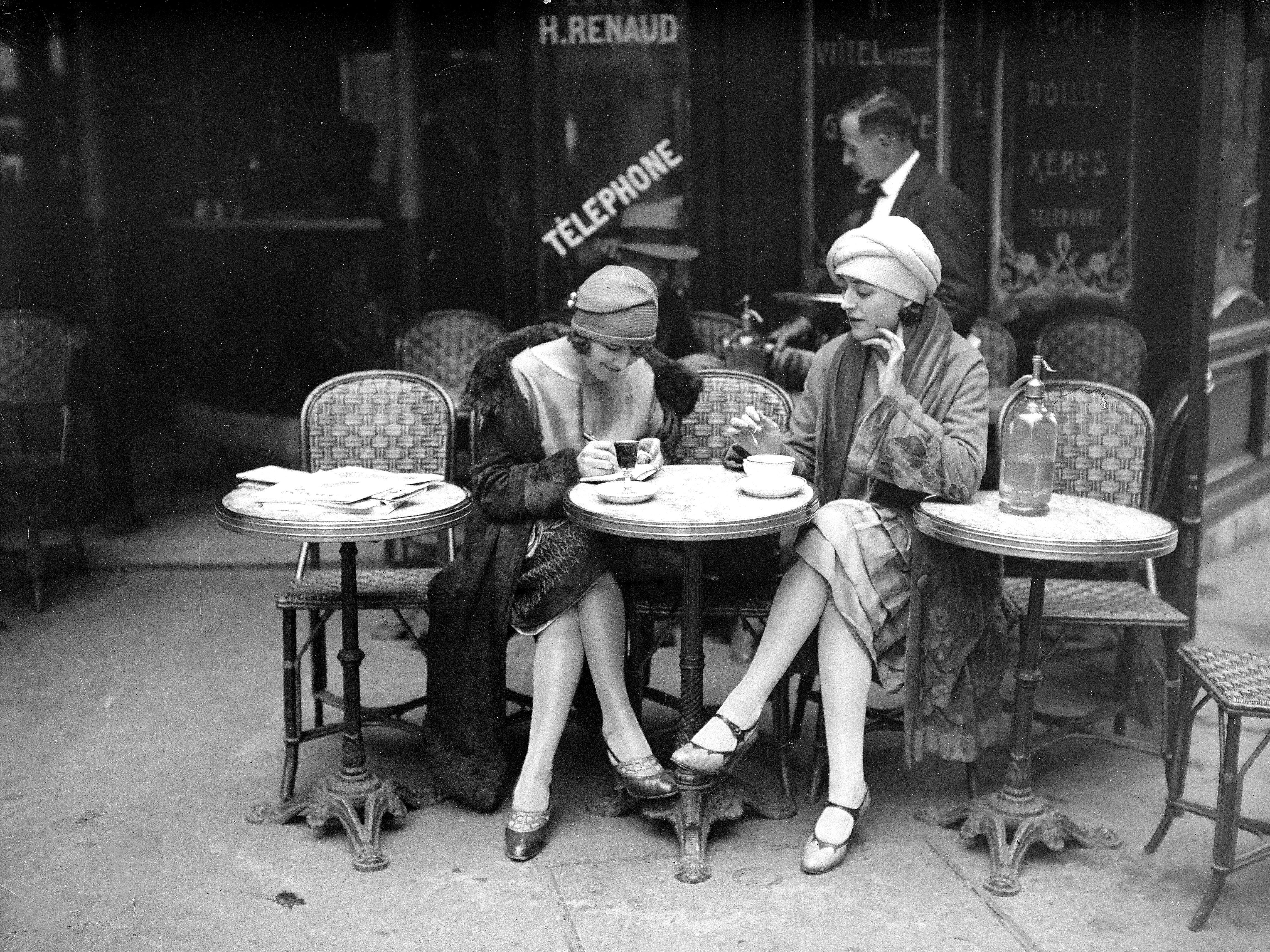 Two women sit at an outdoor café table in Paris in 1920.