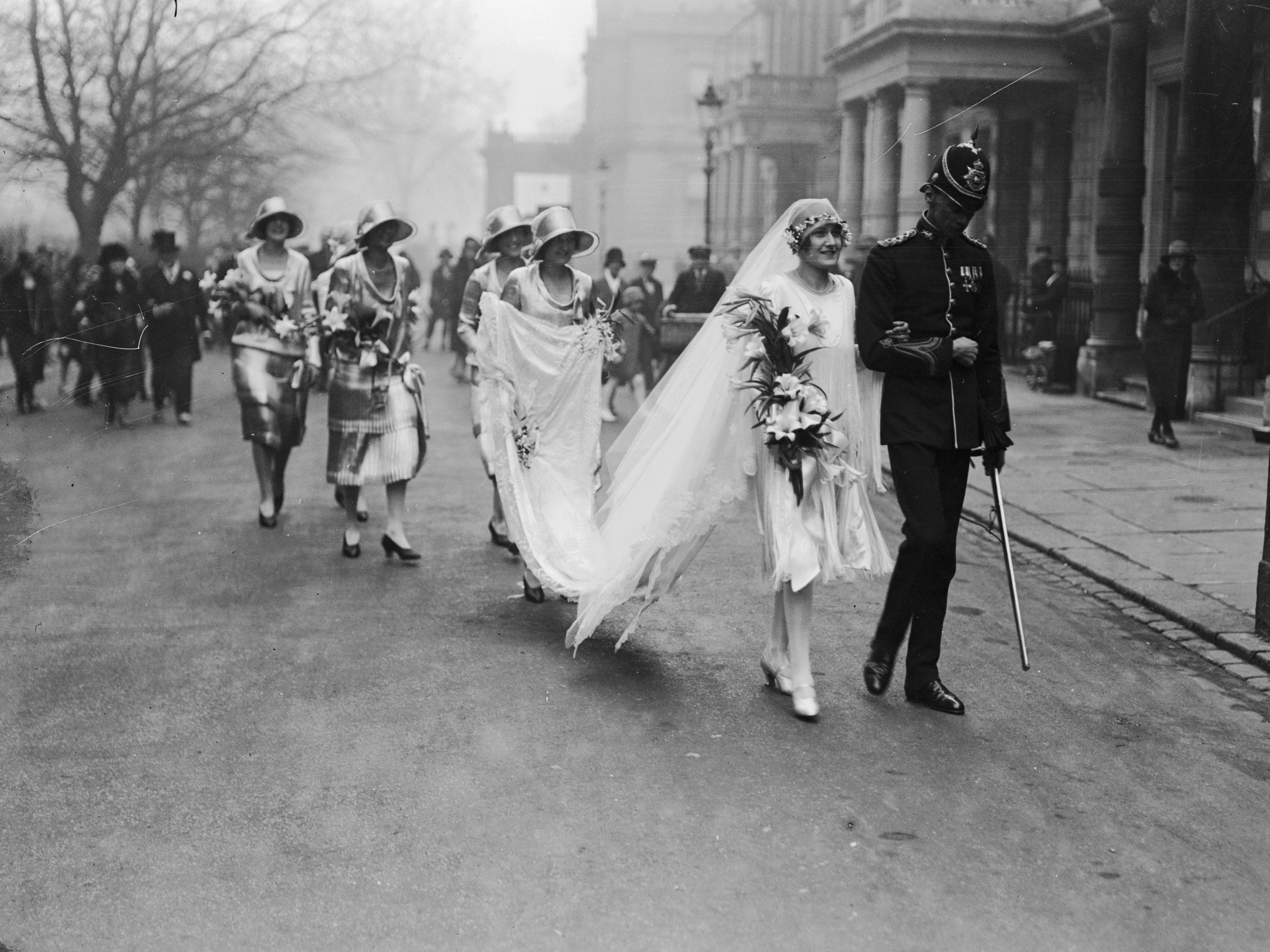 Captain W Howard Green and Irene Harman were married in London in 1928. Harman wore a mid-length white gown with a long veil. Her bridesmaids are seen in the background in matching dresses.