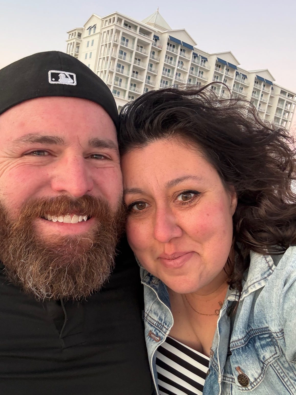 A selfie of a couple with an apartment building in the background.