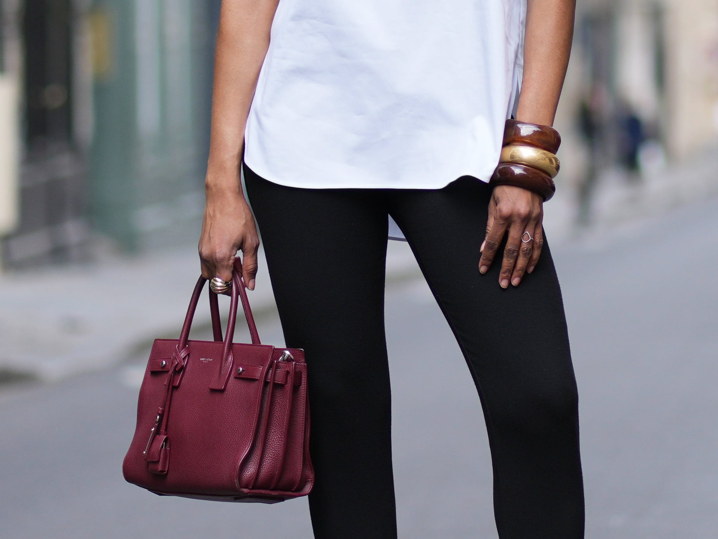 A woman wearing large bangle bracelets and holding a burgundy leather purse.
