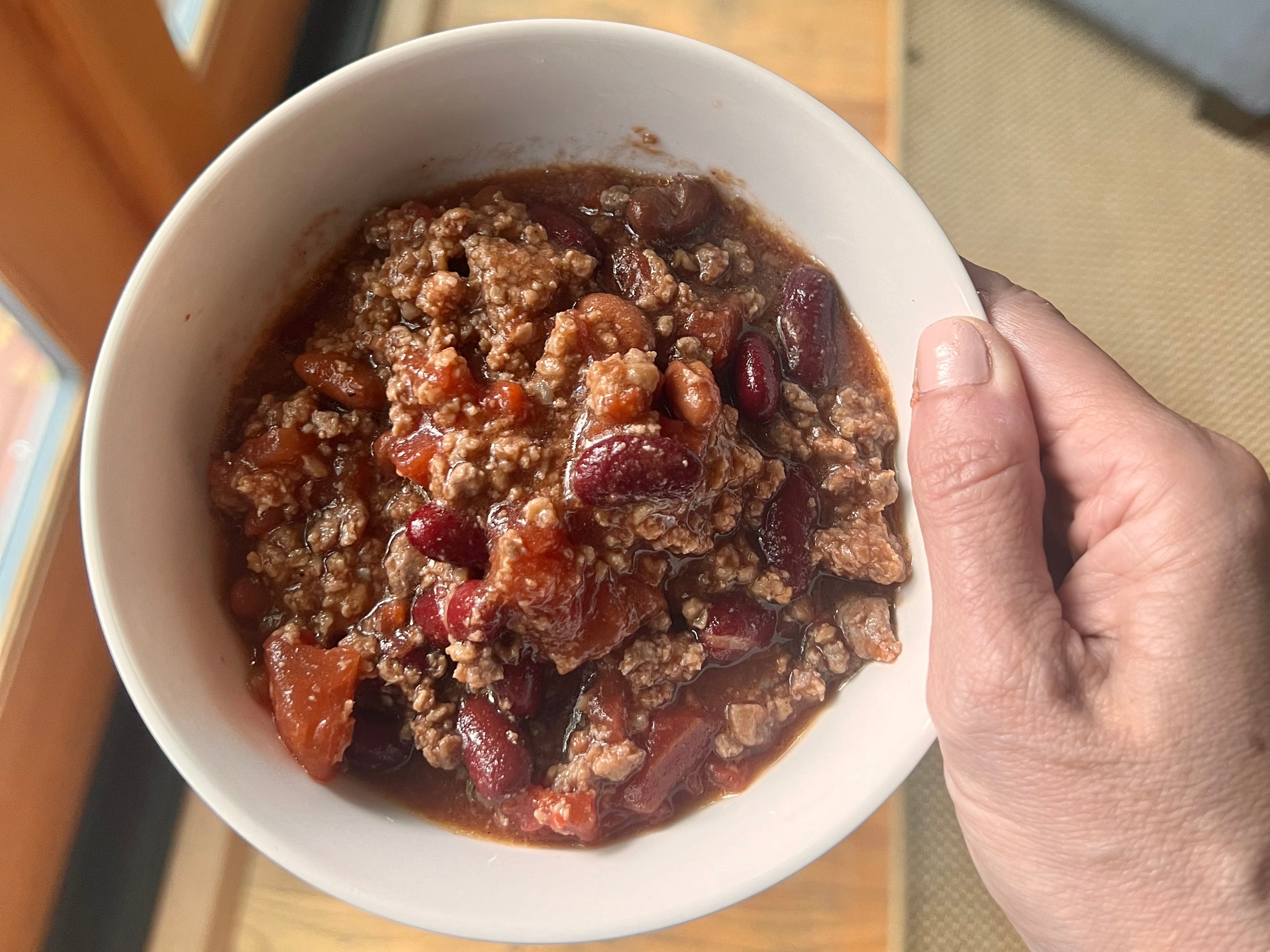 hand holding up a bowl of meat and bean chili