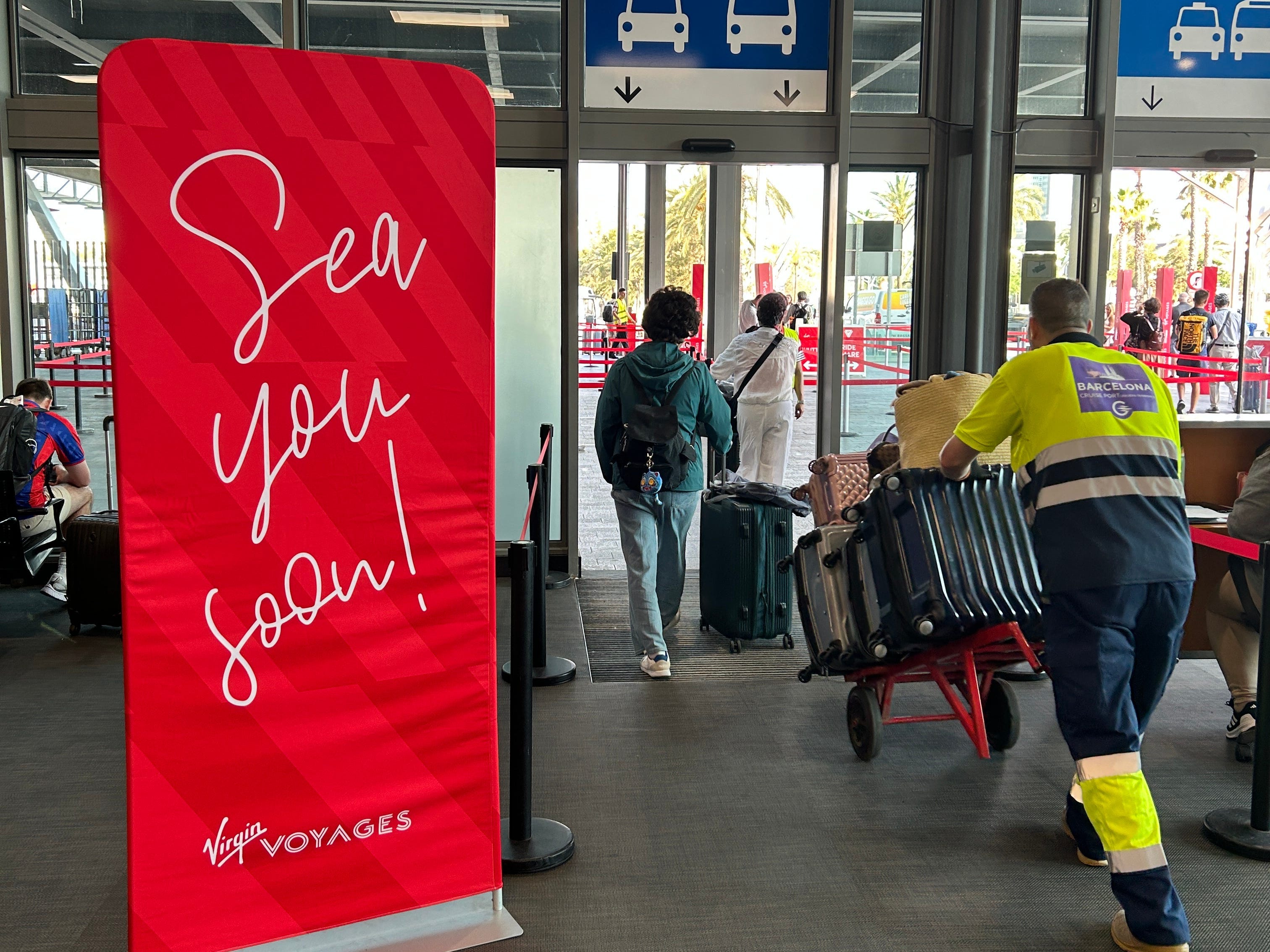 Travelers disembark from a Virgin Voyages cruise ship, with a "See you soon!" sign sitting near the exit.