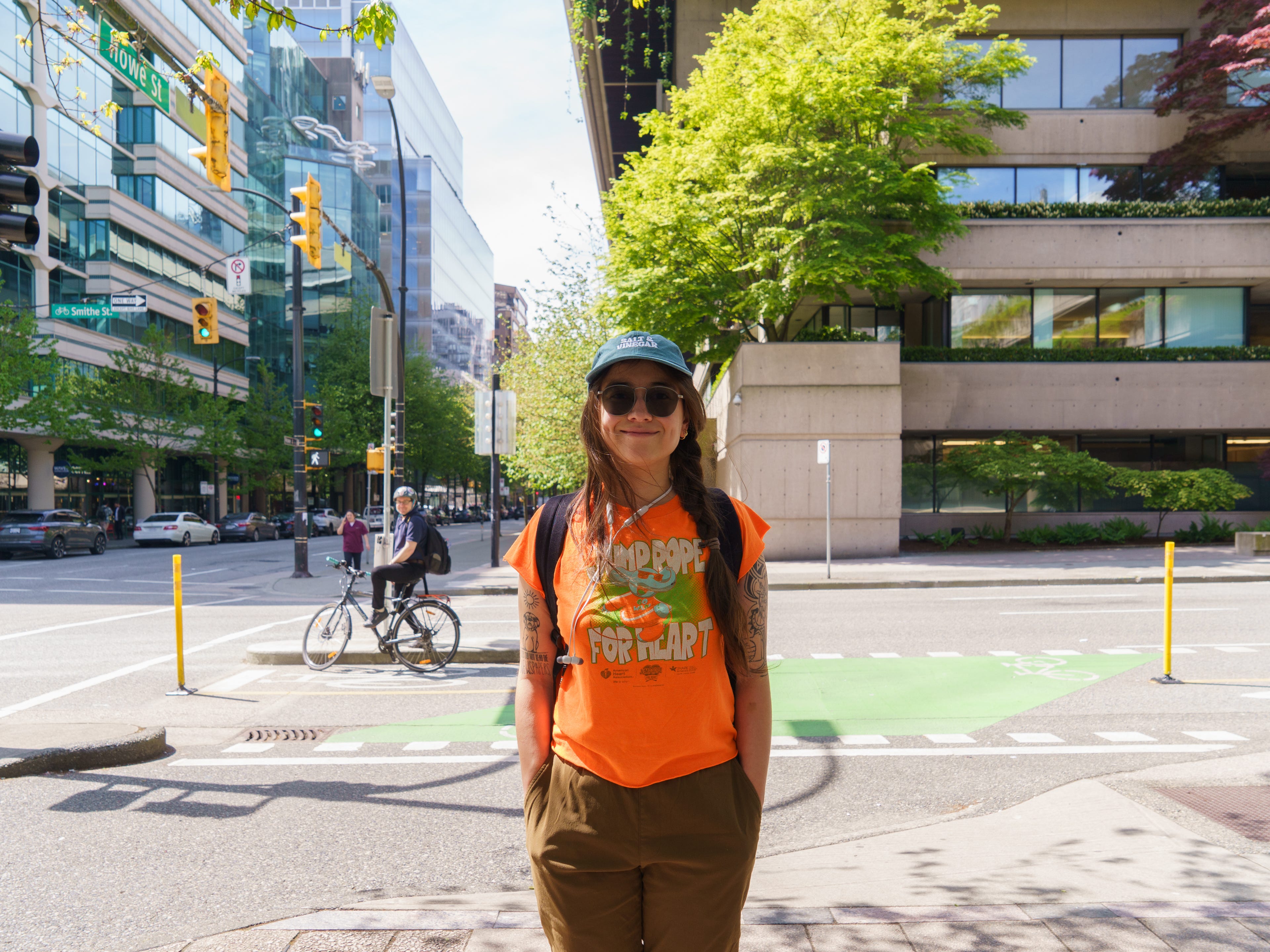Person in sunglasses stands at a downtown intersection with bike lane, traffic lights, and Howe St sign.