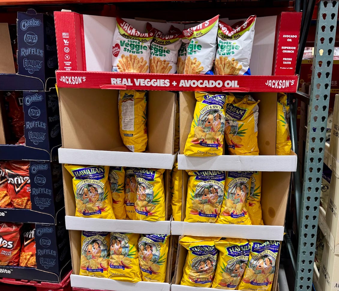 Snack aisle display shelves hold Jackson's veggie straws and Hawaiian kettle style potato chips in yellow bags.