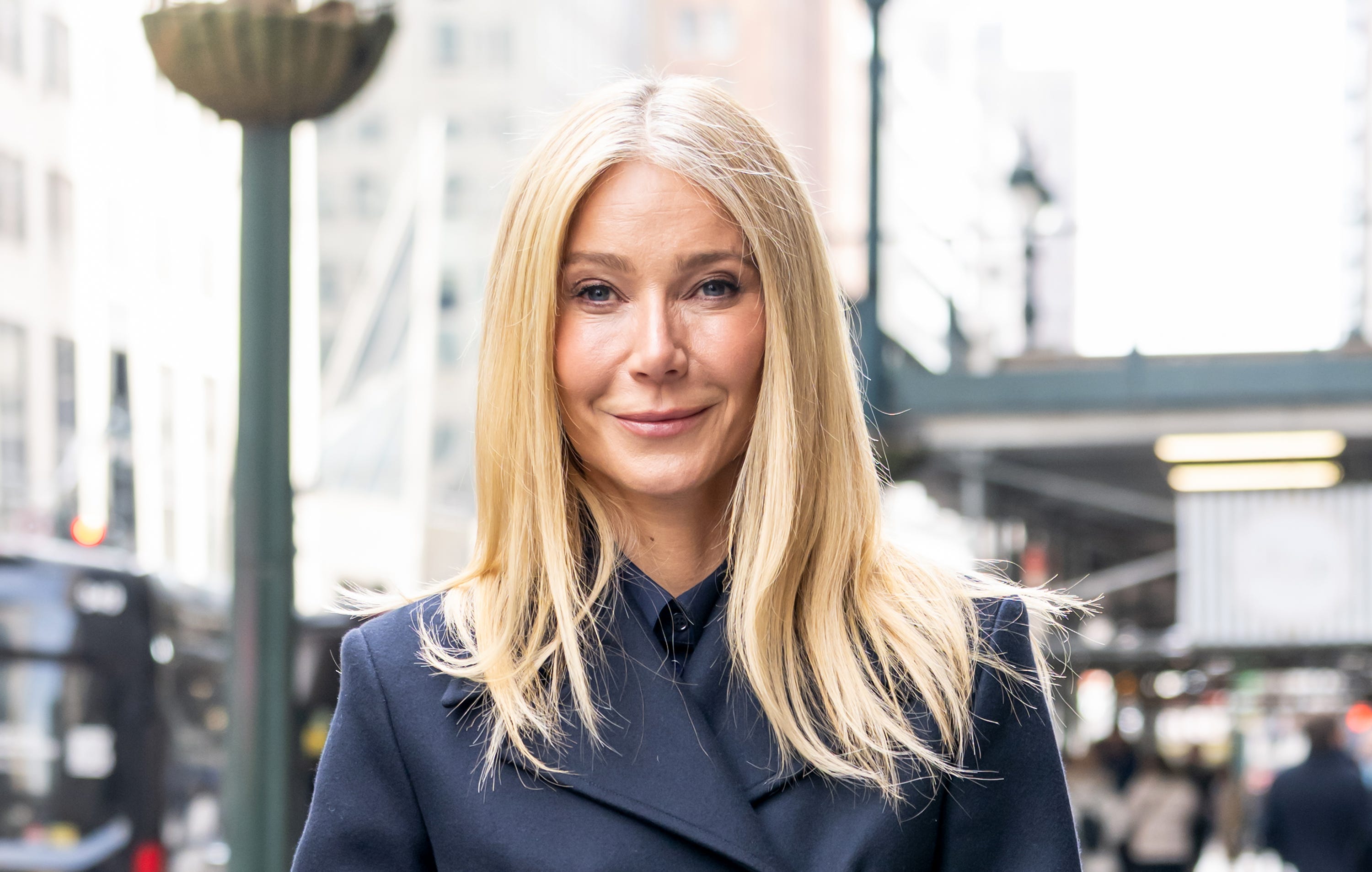 Gwyneth Paltrow stands outside on the street in a navy blue blazer.