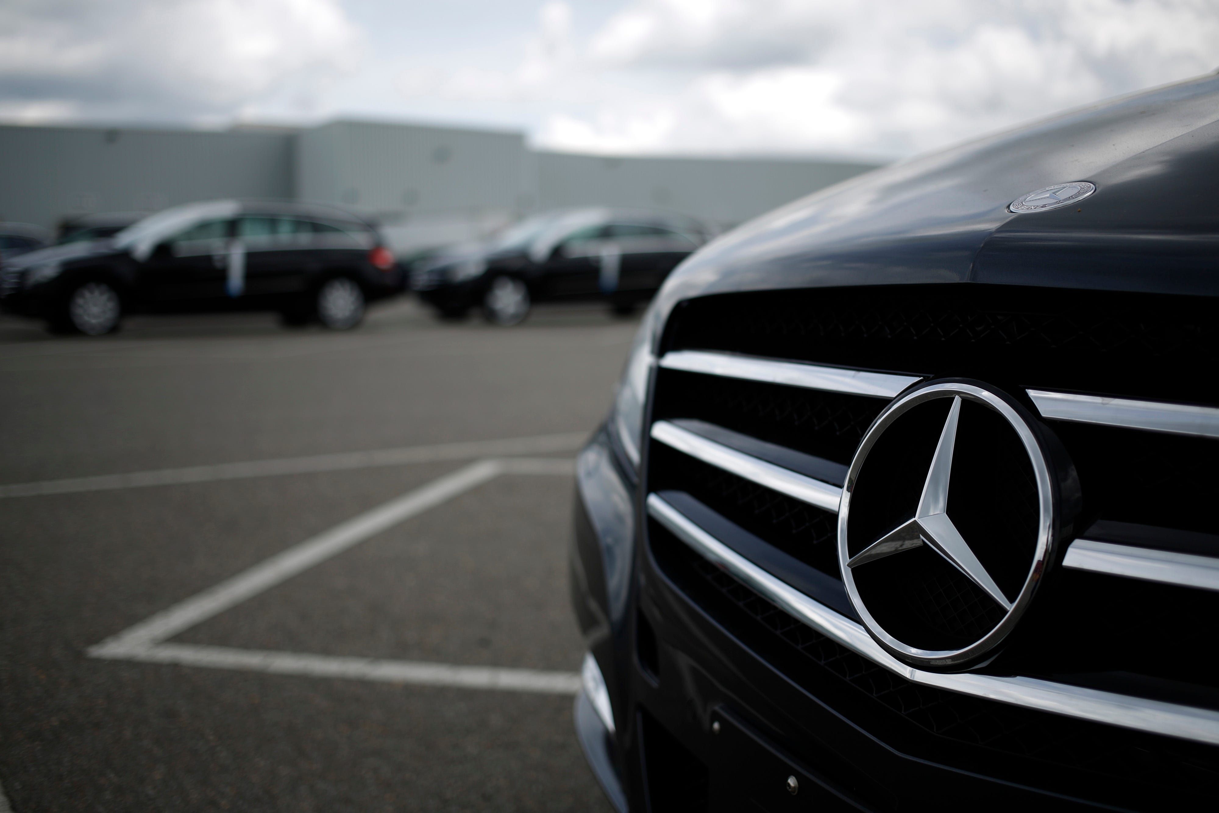 Close-up of a Mercedes-Benz grille and emblem on a black vehicle in a parking lot with other cars behind.
