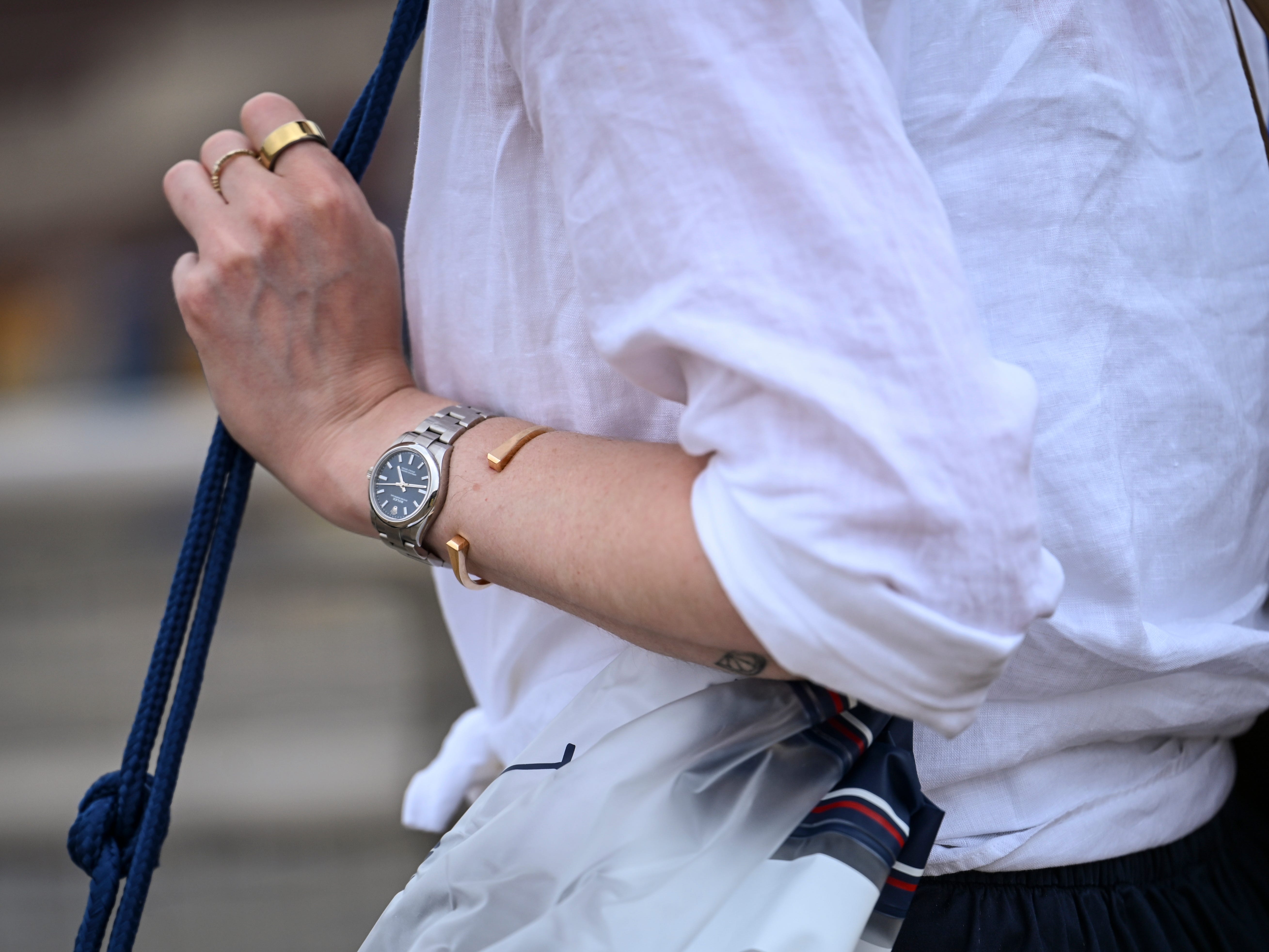 Close-up of a person in a white shirt wearing rings, a bracelet, and a wristwatch while holding a blue strap.